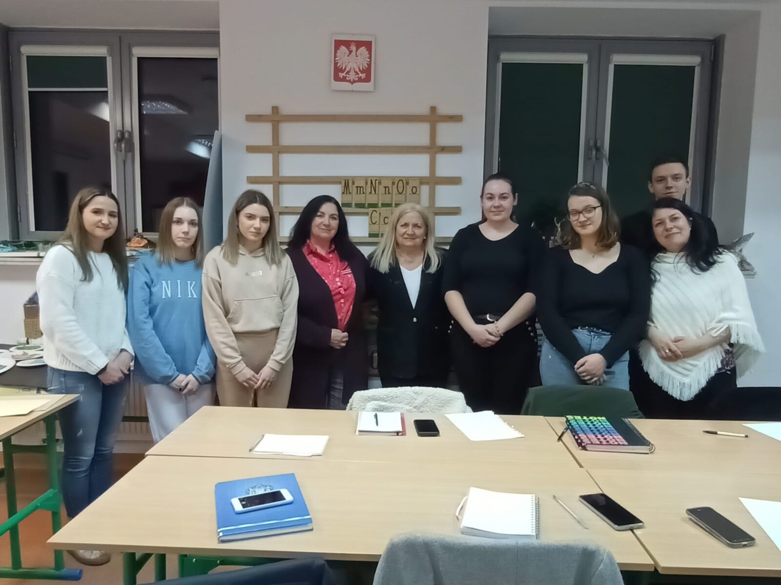 Wspólne zdjęcie studentów pedagogiki z opiekunem koła naukowego. Przed nimi stoły z notatkami studentów.