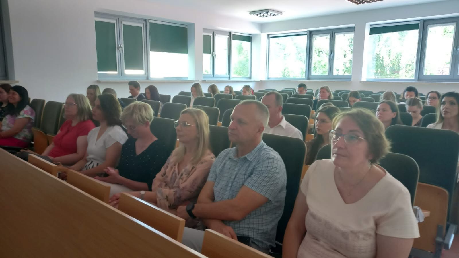 Uczestnicy konferencji słuchają wystąpienia. na pierwszym planie wykładowcy akademiccy, za nimi studenci siedzący na auli.